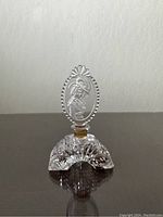 Front view of the crystal perfume bottle showing the detailed etched portrait of the woman on the oval stopper and intricate cut design on the base.