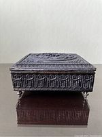 Close-up front view showing the side relief and small rounded feet on which the box stands.