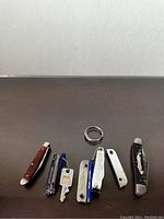 Top-down photo of seven items lined up including five pocketknives/pocketcutters, a metal ring, and a key attached to one cutter.
