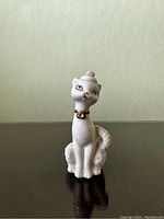 Front view of the vintage porcelain cat figurine displaying its elegant shape, gold collar, and textured tail.