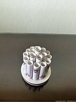 Top angled view showing the circular arrangement of 19 vertical porcelain tubes with pink rose decorations and a white base.