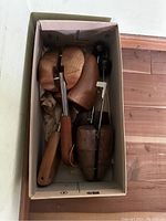Four vintage wooden shoe trees with metal adjustable parts, stored in a box, showing varied wood colors and handles.