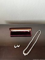 Photo of the vintage white bead necklace with sterling silver clasp, matching white carved clip-on earrings, and burgundy velvet presentation box lid.