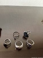 Front view of all five rings arranged in a semicircle on a reflective surface showing stones and metalwork.