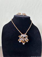 Front view of yellow and clear rhinestone necklace with matching earrings on black display bust.