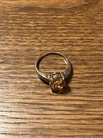 Top-down photo of the ring on a wooden surface showing the oval yellow stone and prong setting.