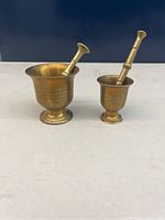 Two miniature brass mortar and pestle sets on a white surface against a dark background.