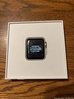 Apple Watch Series 3 displaying low battery message inside the original white Apple Watch box on wooden surface.