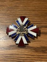 Photo of a 3x3 inch metal cross badge featuring red, white, and blue enamel sections and a central coat of arms with lions.