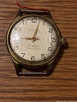 Front view of Cardinal vintage wristwatch showing aged white dial with gold-tone numerals and hands, visible wear and patina.