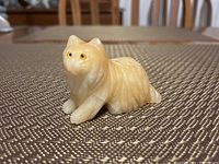 Single yellow-toned carved stone cat figurine with detailed carved fur and painted yellow eyes shown on a fabric surface