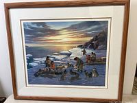 Framed Inuit-themed art print showing a winter scene with Inuit people, dogs, and a sunset behind an icy landscape, signed by Nori Peter.