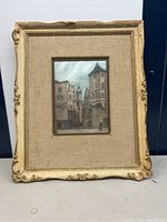 Framed painting on silk showing a European street scene with a clock tower in the distance.