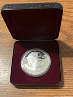 Opened presentation case showing silver dollar coin inside a round protective capsule, velvet-lined interior.