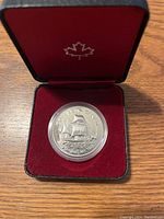Close-up of 1979 Canadian silver dollar coin featuring a sailing ship design, secured in a protective capsule inside a red velvet-lined presentation case with a maple leaf emblem.
