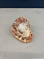 Photo of a small carved conch shell showing a white cameo profile of a woman on the brown shell surface.