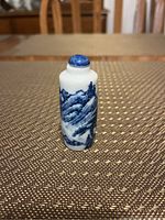 Snuff bottle showing detailed landscape design in blue on white porcelain and blue rounded cap.