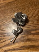 Photo of a sterling silver rose brooch placed flat on a wooden surface showing front and side angles.