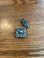 Photo of open sterling silver case showing ornate embossed floral and scroll design and hinged lid with chain loop