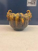 Front view of Victorian style Mejolica flower pot showing ornate raised floral designs and sculpted handles with a glossy finish.