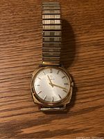 Front view of a vintage Lanco mens wristwatch with gold-tone metal case and stretch band on a wooden surface.