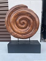 Front view of wooden spiral sculpture on black base showing detailed carved swirls.