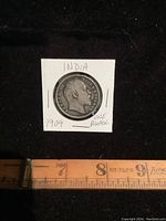 Front side of 1904 India One Rupee coin showing King Edward VII portrait with surrounding inscription. Coin is secured in a white cardboard holder with handwritten notes and ruler indicating size.