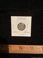 Front view of the 1957 India 2 Paise coin placed on black background with a ruler underneath for scale.