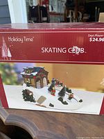 Box with branding Holiday Time Skating Club and image showing the winter skating scene with chalet, skaters on the rink, and trees covered in snow.
