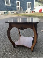 Side view of antique wooden parlour table showing curved legs, decorative apron, lower shelf, and scalloped shaped top edges