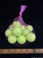 Twelve yellow golf balls in a pink mesh bag shown next to a ruler for scale.