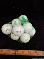 Twelve white Polara golf balls in a green mesh bag, arranged with a ruler for size reference.
