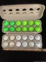 Top-down view of two open egg-carton style trays with 12 neon green and 12 white golf balls arranged in rows. Brands visible include MOJO and Callaway on neon balls and Bridgestone, Titleist, and other brands on white balls. Condition shows light usage.