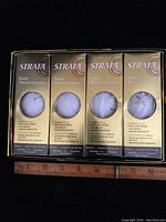 Four boxes of Strata Tour Professional white golf balls, each box containing three balls visible through front window.