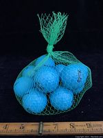 Six blue golf balls in a green mesh net, showing scale against ruler