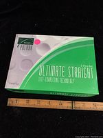 Closed box of Polara Ultimate Straight golf balls with green and white design and pink dot sticker with ruler showing size.