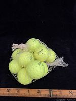 Photo showing dozen yellow Titleist golf balls inside a white mesh net, placed on a black background with a ruler showing approximate size.