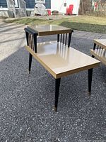 Photo showing one of the 2-tier Marlite side tables with beige laminate surface, black spindle supports, and black tapered legs with brass feet.