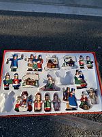 Top-down photo showing full set of 16 vintage wooden Christmas tree ornaments arranged in molded plastic tray inside box, box edges red with white interior.