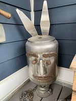 Side view of yard art sculpture showing cylindrical metal face with metal ear pieces extending upwards