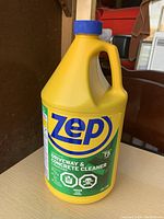 Front view of yellow gallon jug of ZEP Driveway & Concrete Cleaner with blue cap and green label.