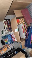 Lot of board games in various boxes including Monopoly, Uno, and puzzle games alongside collectible model cars in display packaging.