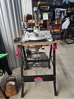 Front view of Jobmate compound mitre saw on stand with red clamps and power cord.