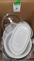 Stack of white oval and round CorningWare dishes with clear glass lids