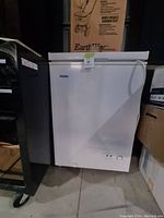 White Haier chest freezer shown from front in storage area with adjacent boxes