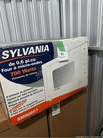 Photo shows original box of Sylvania SM80601 microwave oven with specifications and features, including 700 watts power, 0.6 cu. ft capacity, 6 power levels, manual timer, and glass turntable.