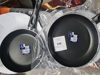 Two black frying pans with non-stick surfaces and ergonomic handles placed side by side in packaging.