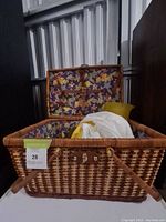 Photo of the picnic basket open, showing the interior fabric lining with a leaf pattern and some contents inside including a yellow fabric item and white plastic or cloth.