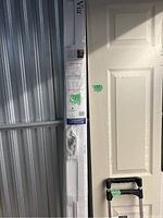 Two brand new sealed screen doors leaning against a wall in original packaging, showing white frame and hardware sealed inside.