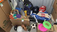 Overhead shot showing tennis rackets, helmets, paddles, bats and frisbees in storage unit.